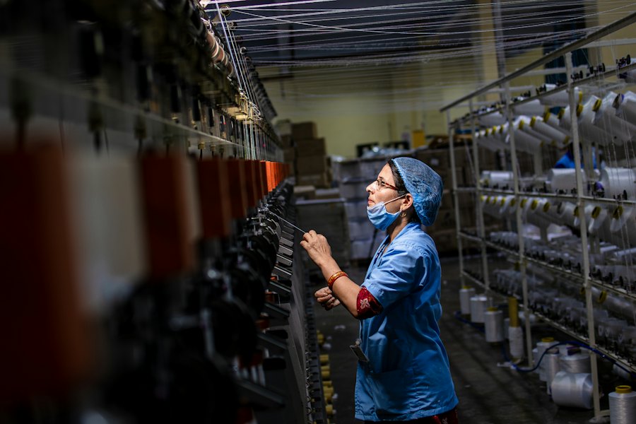 A factory worker checking thread on a production machine
