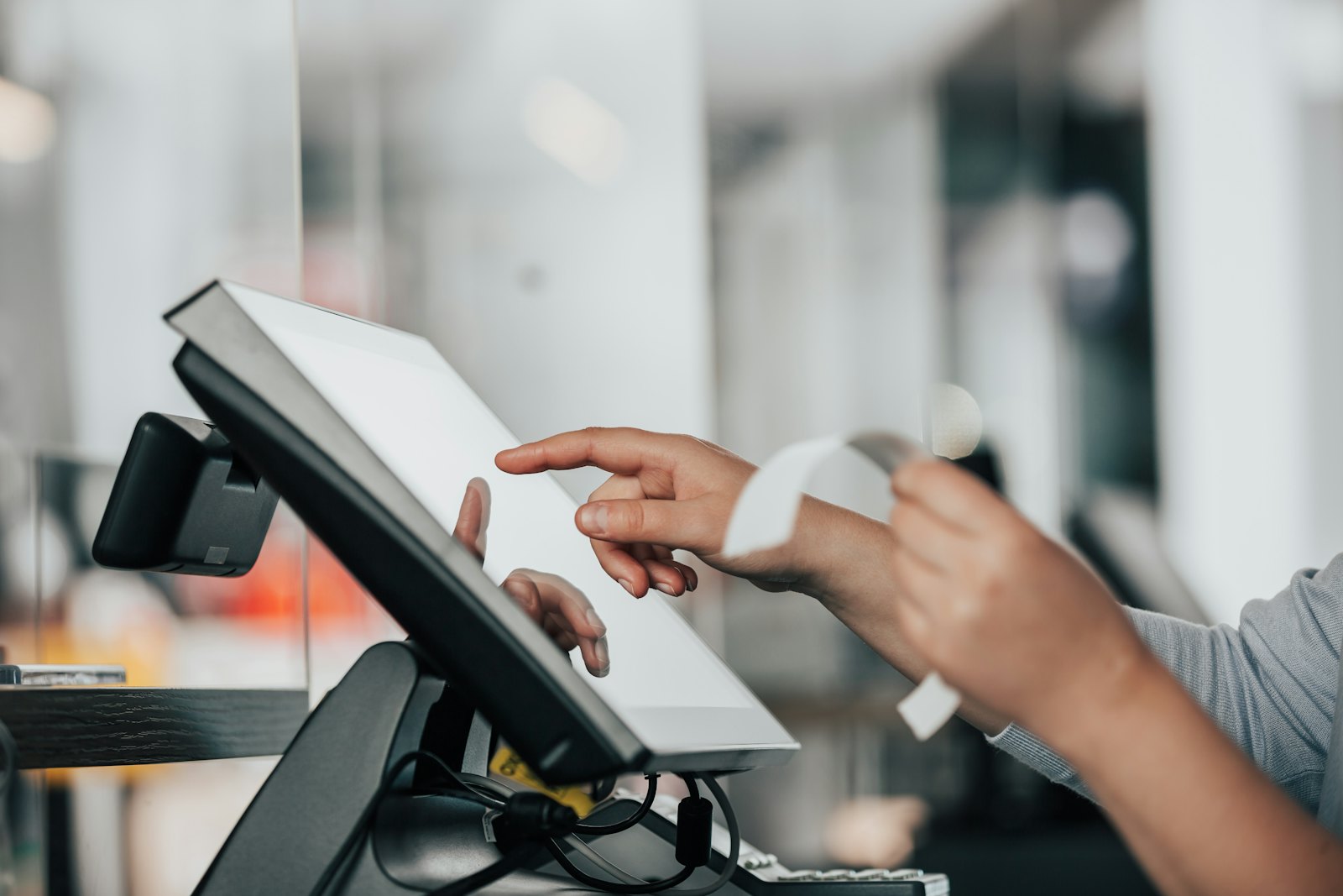 A cashier tapping a point-of-sale screen while tearing off a receipt