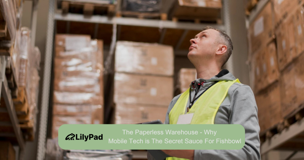 Warehouse worker in a high-visibility vest looks up at tall shelves stacked with boxes.