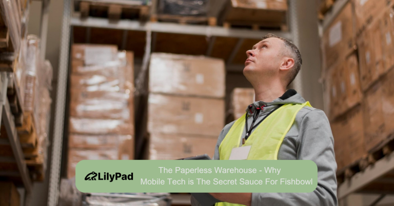 Warehouse worker in a high-visibility vest looks up at tall shelves stacked with boxes.