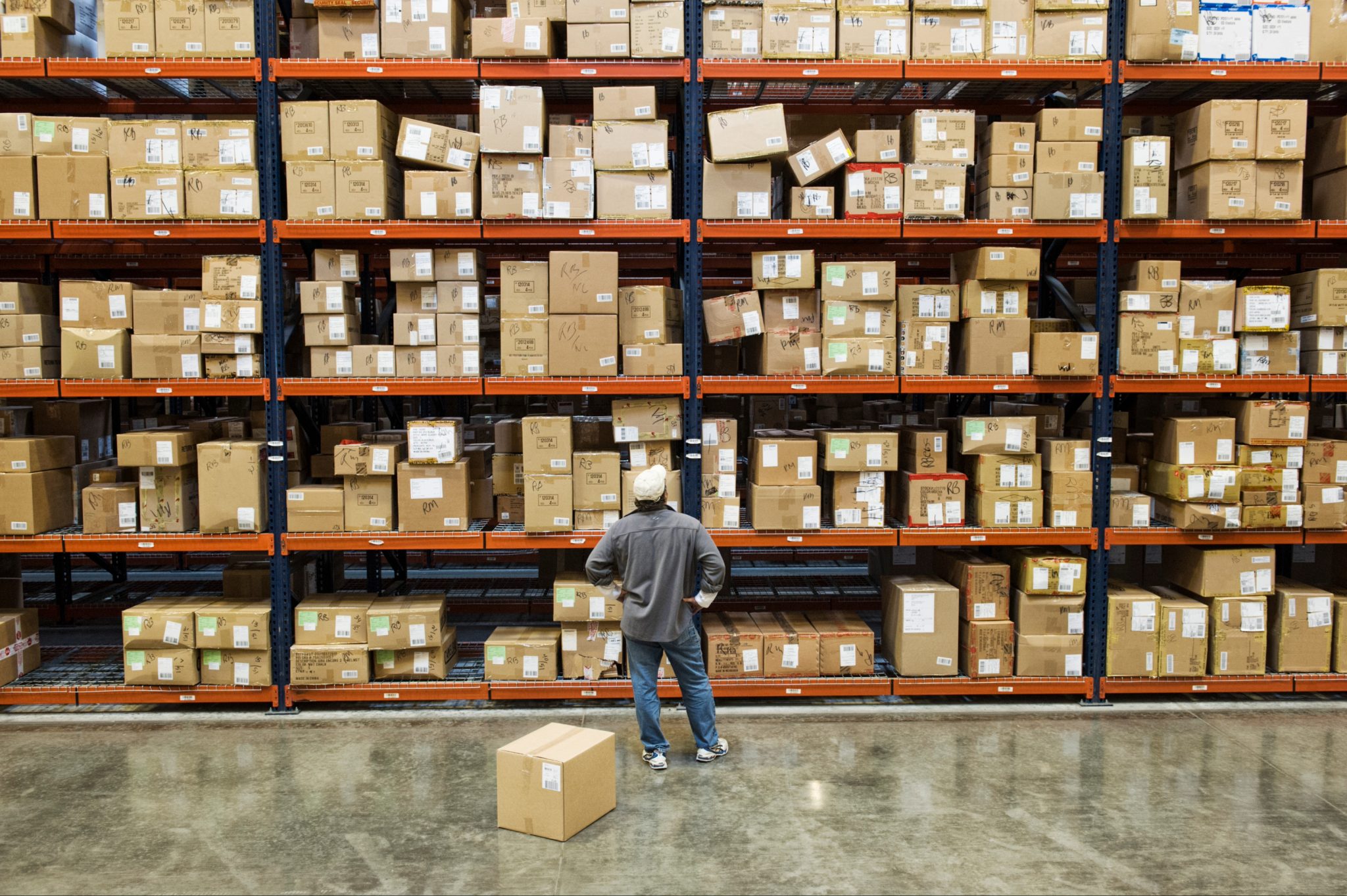 A warehouse worker checking stock in front of a towering wall of shelving